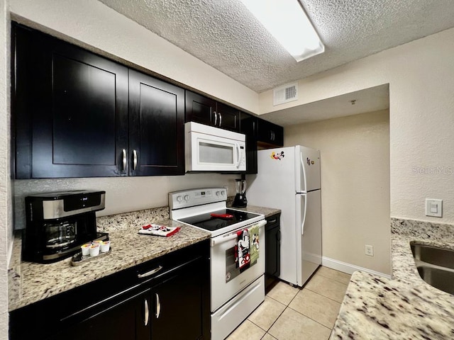 kitchen with light stone countertops, white appliances, light tile patterned floors, and a textured ceiling