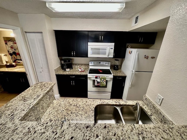 kitchen with white appliances, light stone countertops, sink, and a textured ceiling