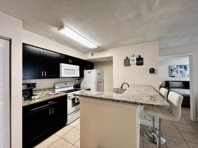 2210 Grand Cayman Ct Unit 1722, Kissimmee, FL 34741 - kitchen featuring white appliances, dark cabinets, a peninsula, a kitchen breakfast bar, and a textured ceiling