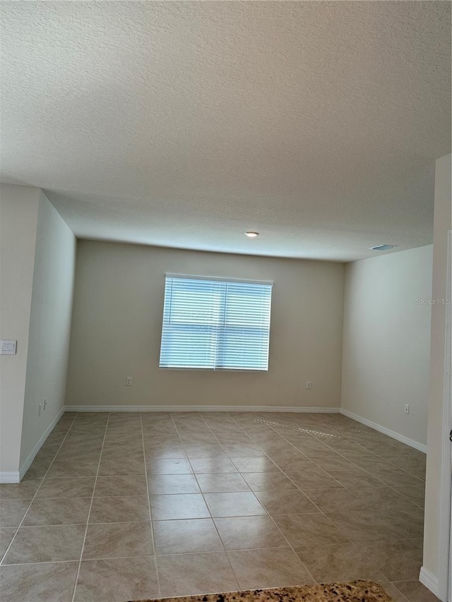 empty room with a textured ceiling and light tile patterned flooring