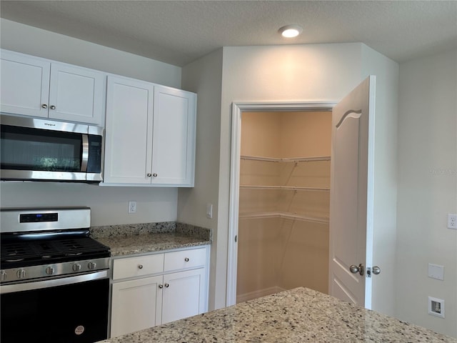 kitchen with light stone countertops, appliances with stainless steel finishes, a textured ceiling, and white cabinets