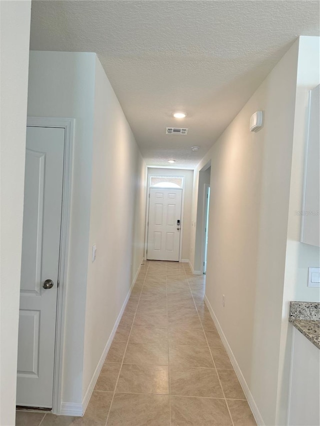 hall featuring a textured ceiling and light tile patterned flooring