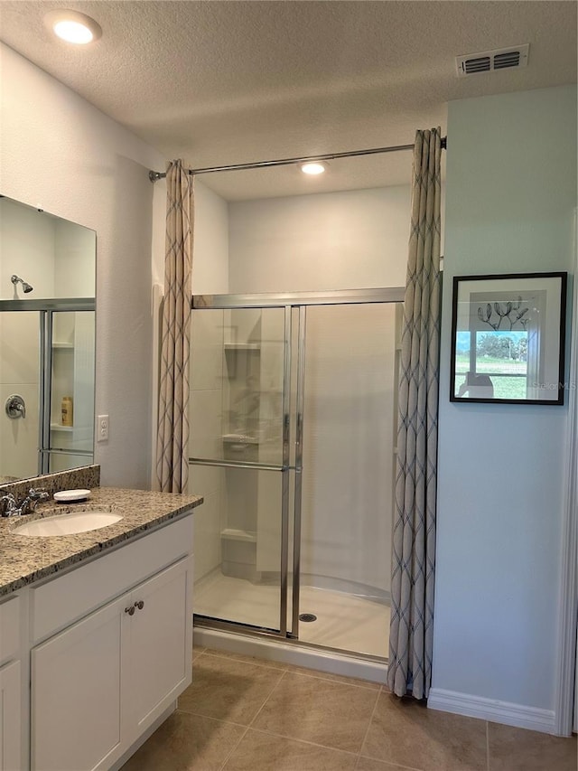 bathroom featuring vanity, a textured ceiling, walk in shower, and tile patterned flooring