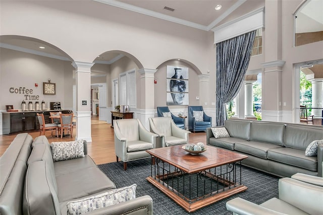 living room with ornate columns, wood-type flooring, ornamental molding, and high vaulted ceiling