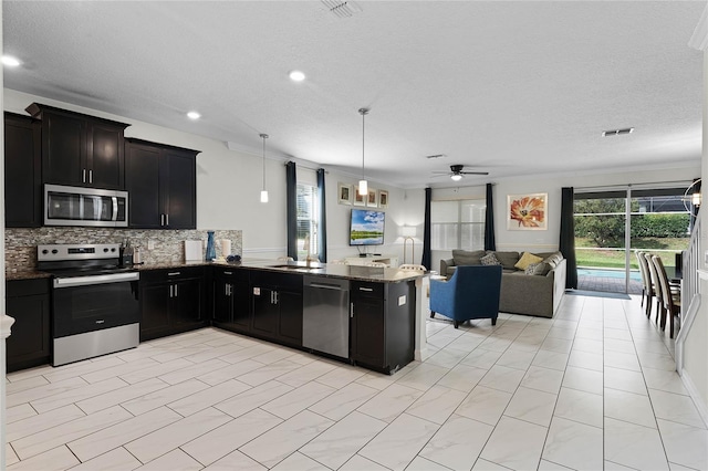 kitchen featuring appliances with stainless steel finishes, stone countertops, kitchen peninsula, hanging light fixtures, and decorative backsplash