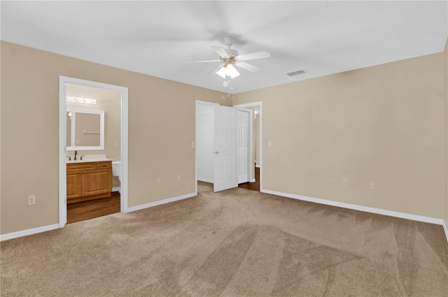 unfurnished bedroom with ensuite bathroom, a spacious closet, light colored carpet, a closet, and ceiling fan