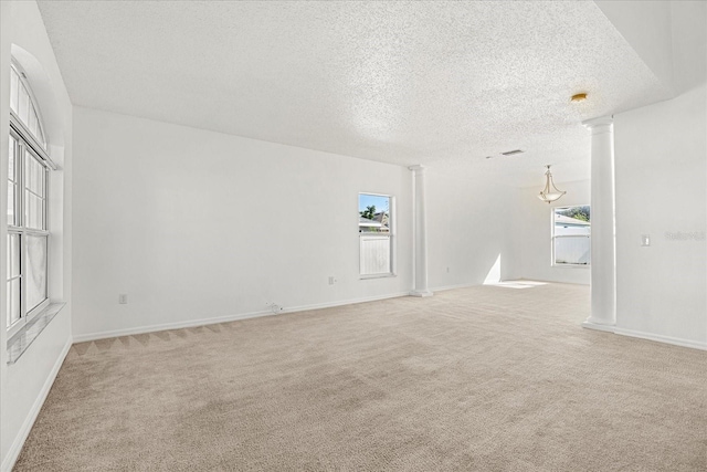 carpeted spare room featuring decorative columns and a textured ceiling