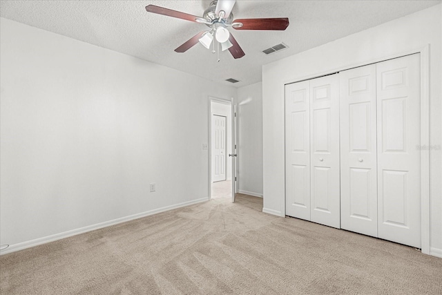 unfurnished bedroom with ceiling fan, light colored carpet, a textured ceiling, and a closet