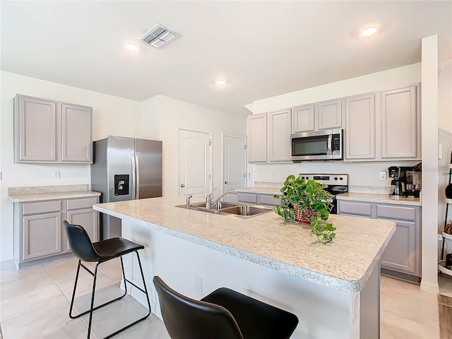 kitchen featuring sink, stainless steel appliances, gray cabinets, a breakfast bar area, and a center island with sink