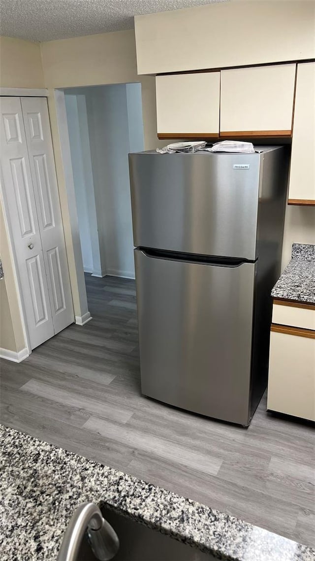 kitchen featuring a textured ceiling, stainless steel fridge, light hardwood / wood-style floors, and white cabinetry