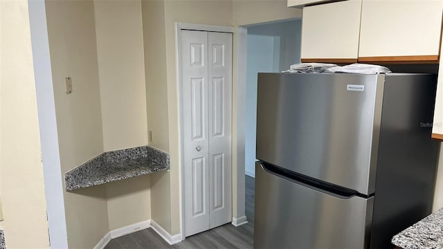 kitchen featuring wood-type flooring, white cabinets, stainless steel fridge, and light stone counters