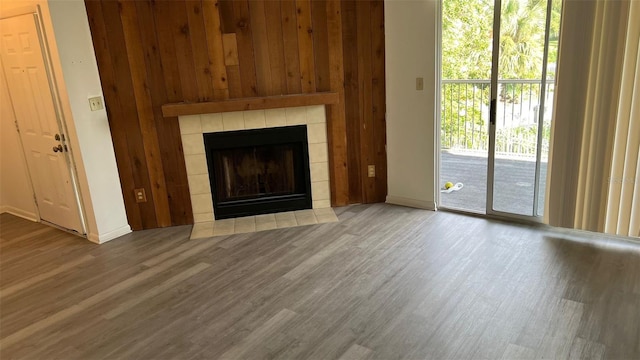 unfurnished living room with wood walls, hardwood / wood-style floors, and a tiled fireplace