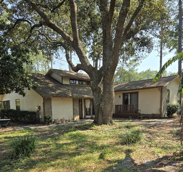 view of front of house featuring roof with shingles, brick siding, and a deck