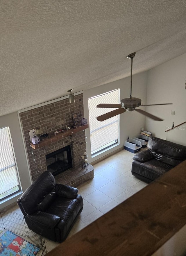 living area featuring tile patterned flooring, a textured ceiling, a ceiling fan, and a fireplace