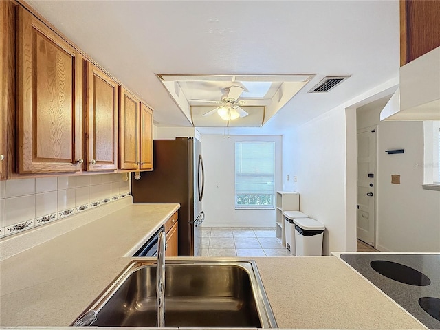 kitchen featuring ceiling fan, a skylight, a raised ceiling, sink, and backsplash