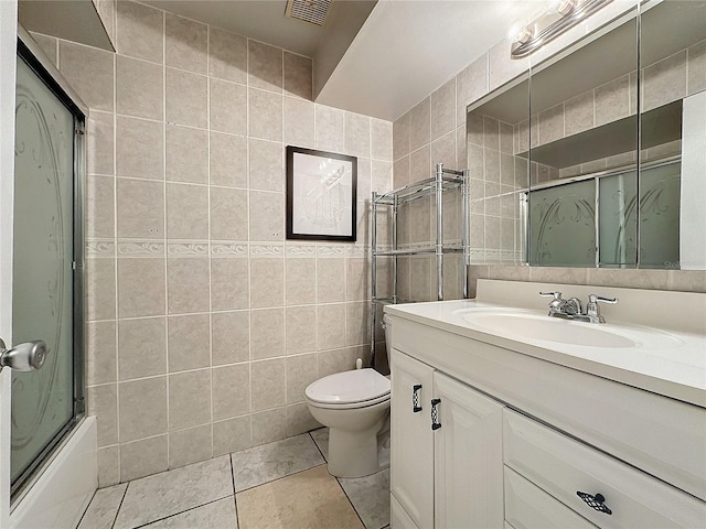 full bathroom with vanity, toilet, bath / shower combo with glass door, tile walls, and tile patterned flooring