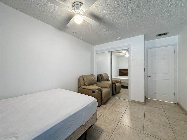 bedroom featuring ceiling fan, a textured ceiling, a closet, and light tile patterned flooring