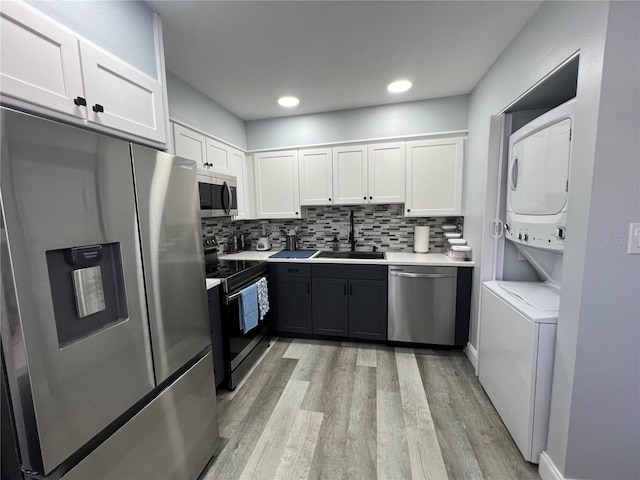 kitchen featuring stainless steel appliances, white cabinets, sink, stacked washer and clothes dryer, and backsplash