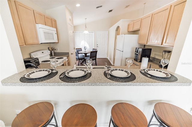 kitchen with lofted ceiling, white appliances, kitchen peninsula, light brown cabinetry, and decorative light fixtures