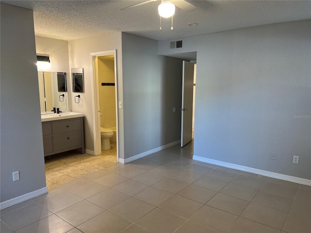 unfurnished bedroom featuring ensuite bathroom, ceiling fan, light tile patterned floors, and a textured ceiling