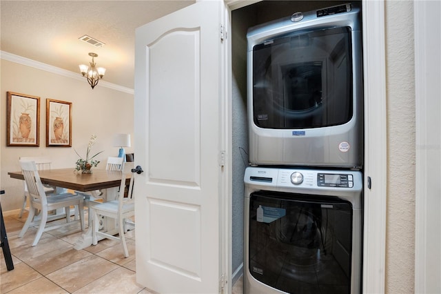 washroom with light tile patterned floors, a textured ceiling, stacked washer / dryer, a notable chandelier, and crown molding