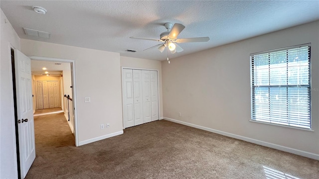 unfurnished bedroom featuring ceiling fan, a textured ceiling, a closet, and carpet