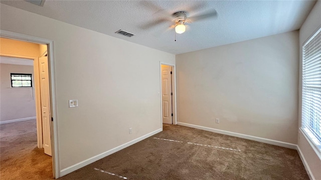 unfurnished bedroom with a textured ceiling, dark colored carpet, multiple windows, and ceiling fan