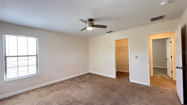 unfurnished bedroom featuring ceiling fan, a textured ceiling, a walk in closet, a closet, and carpet floors