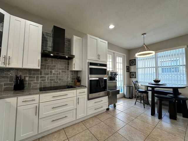 2321 Hinsdale Dr, Kissimmee, FL 34741 - kitchen with wall chimney exhaust hood, black electric cooktop, stainless steel double oven, backsplash, and dark stone countertops