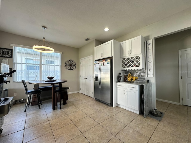 kitchen featuring tasteful backsplash, stainless steel fridge, white cabinetry, decorative light fixtures, and light tile patterned floors