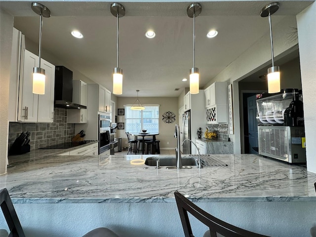 kitchen with light stone countertops, wall chimney range hood, white cabinetry, and decorative backsplash