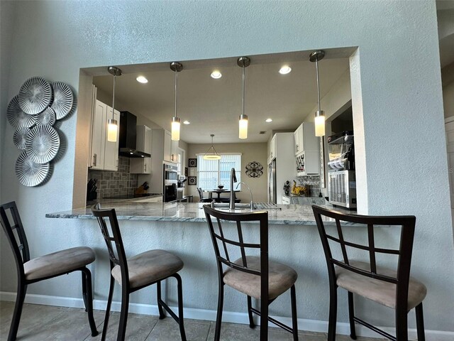 2321 Hinsdale Dr, Kissimmee, FL 34741 - kitchen with wall chimney exhaust hood, a peninsula, backsplash, light stone countertops, and recessed lighting