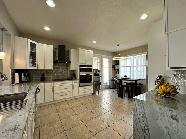 2321 Hinsdale Dr, Kissimmee, FL 34741 - kitchen with wall chimney exhaust hood, double oven, tasteful backsplash, light stone counters, and black electric stovetop