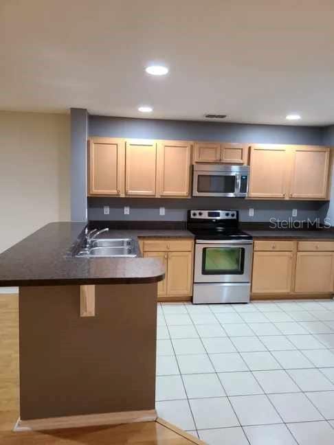 kitchen featuring dark countertops, a sink, stainless steel appliances, recessed lighting, and a peninsula