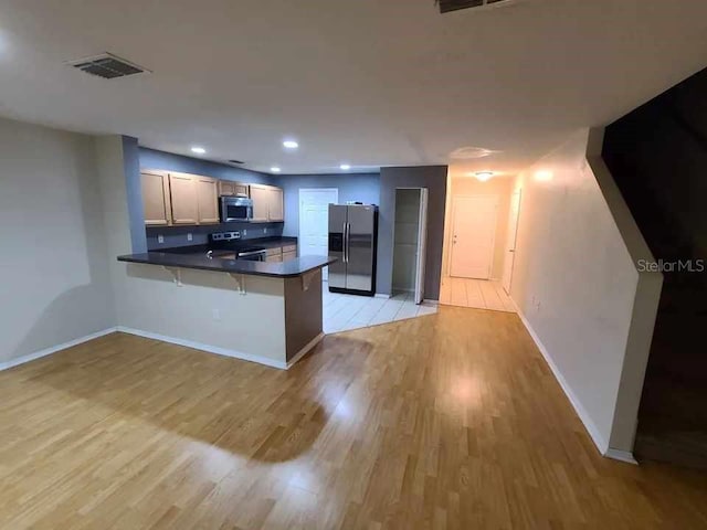 kitchen with visible vents, a peninsula, dark countertops, light wood-type flooring, and appliances with stainless steel finishes