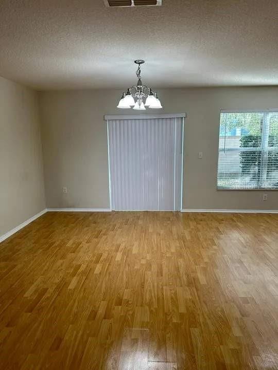 unfurnished dining area featuring a textured ceiling, visible vents, wood finished floors, baseboards, and a chandelier