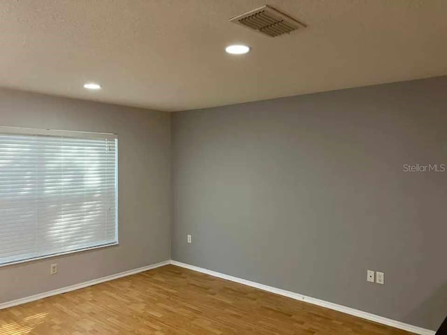 unfurnished room with baseboards, recessed lighting, wood finished floors, and visible vents