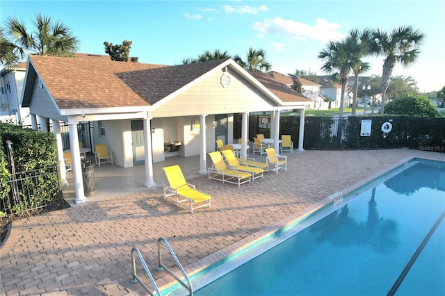 exterior space with a community pool, fence, a patio area, and roof with shingles