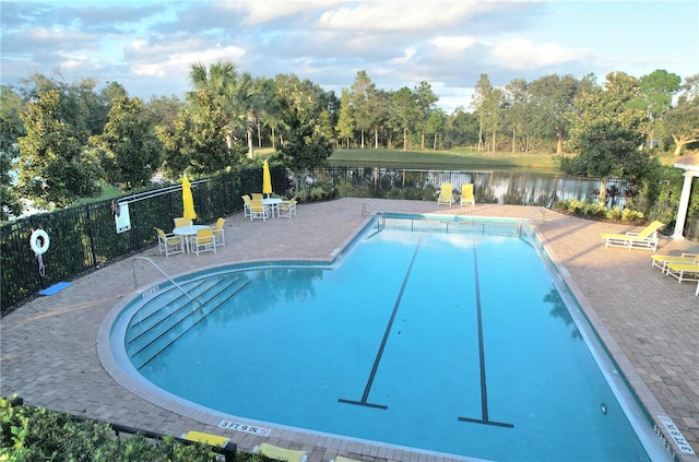 pool with fence, a water view, and a patio area