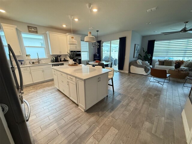 kitchen with pendant lighting, white cabinets, sink, fridge, and a center island