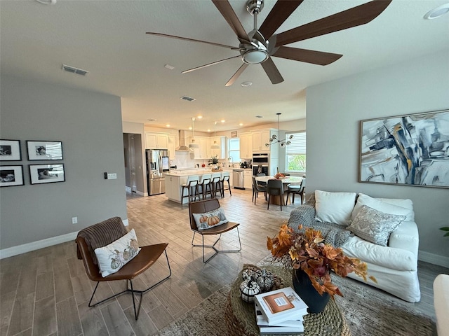 living room with ceiling fan with notable chandelier, sink, and light hardwood / wood-style floors