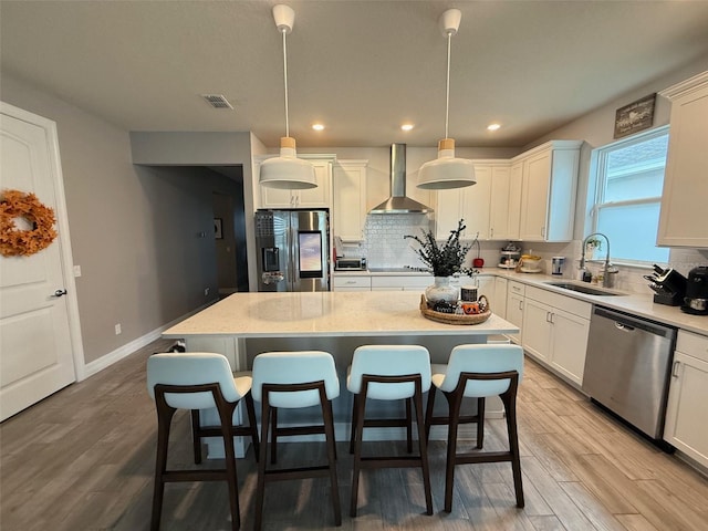 kitchen featuring wall chimney range hood, a kitchen island, decorative light fixtures, sink, and appliances with stainless steel finishes