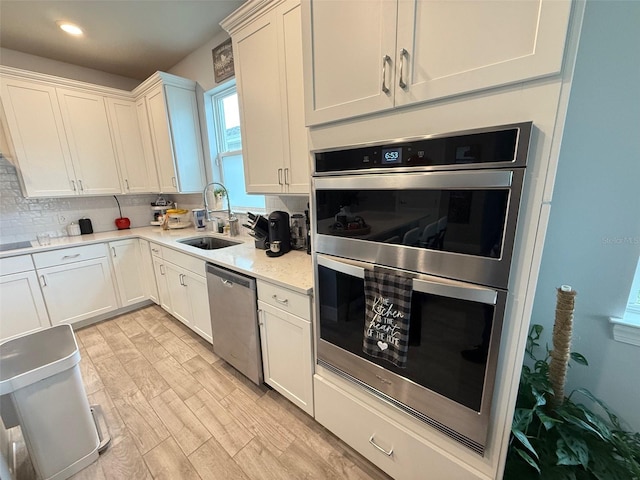 kitchen with white cabinets, sink, light hardwood / wood-style flooring, appliances with stainless steel finishes, and backsplash