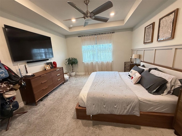 bedroom featuring light carpet, ceiling fan, and a tray ceiling