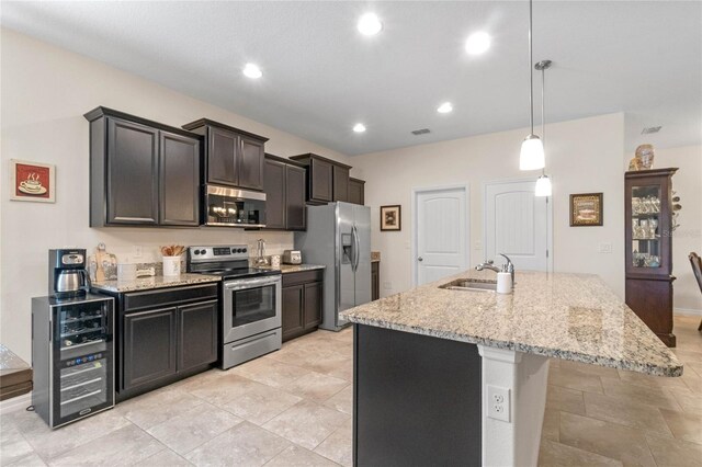 kitchen featuring beverage cooler, decorative light fixtures, a center island with sink, stainless steel appliances, and light stone countertops