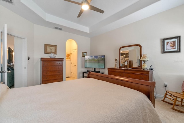 carpeted bedroom featuring ceiling fan, a tray ceiling, and ensuite bath