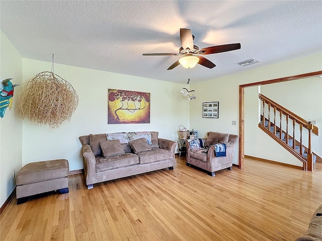 living room featuring ceiling fan, light hardwood / wood-style flooring, and a textured ceiling