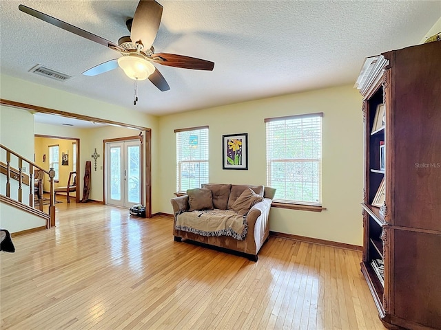 living room featuring ceiling fan, a textured ceiling, french doors, and light hardwood / wood-style floors