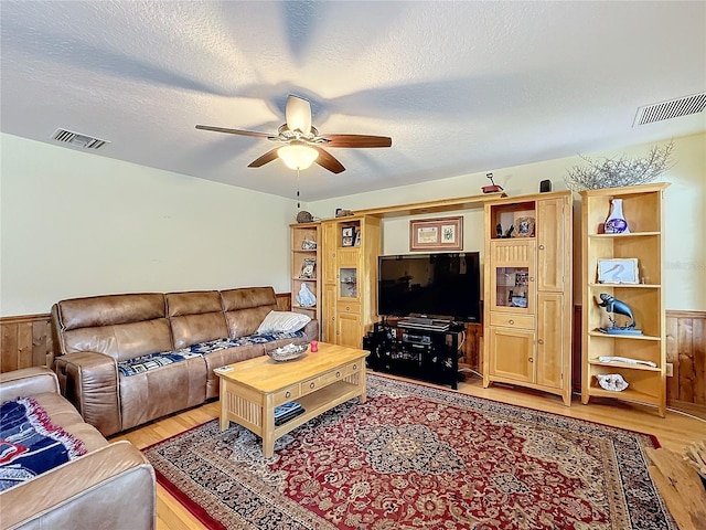 living room with ceiling fan, wood walls, light hardwood / wood-style floors, and a textured ceiling