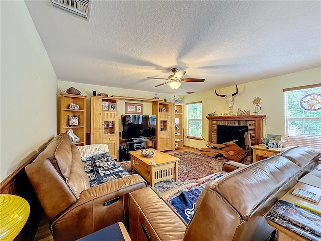 living room with a fireplace, ceiling fan, and a textured ceiling